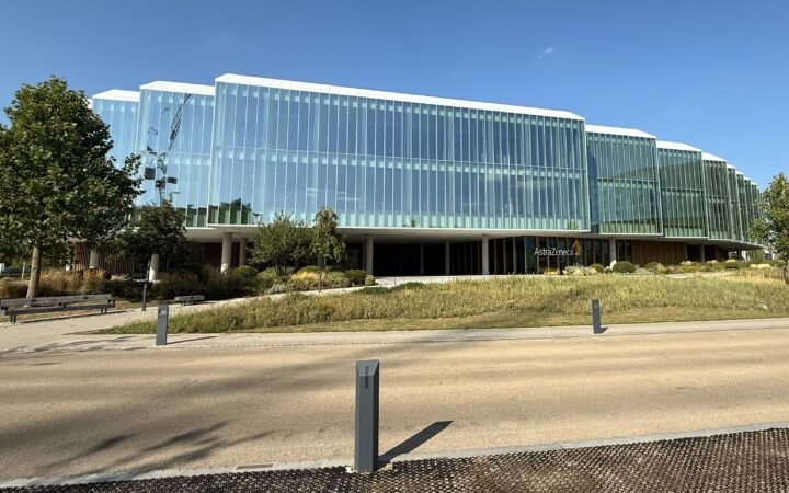 Edifício envidraçado da AstraZeneca em Cambridge, na Inglaterra, com jardins em primeiro plano.