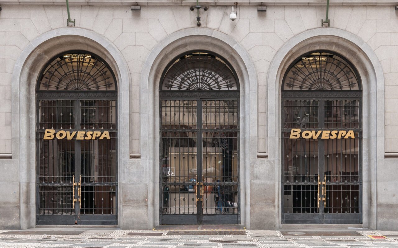 Três portas em arco na fachada da Bovespa, em São Paulo, com o nome da bolsa em letras douradas.