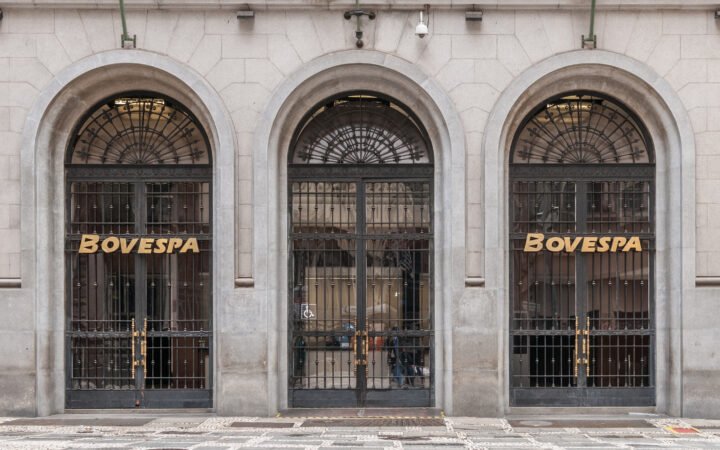 Três portas em arco na fachada da Bovespa, em São Paulo, com o nome da bolsa em letras douradas.