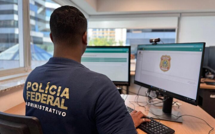 Servidor administrativo da Polícia Federal trabalha diante de dois monitores.