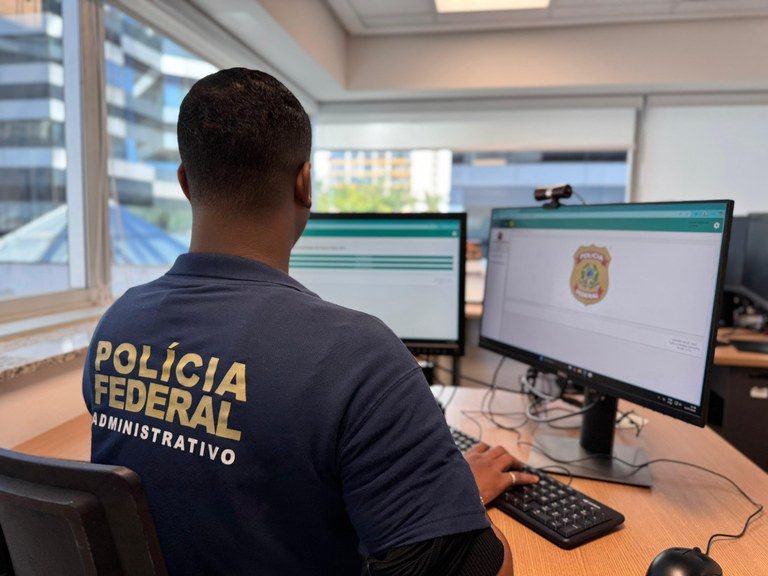 Servidor administrativo da Polícia Federal trabalha diante de dois monitores.