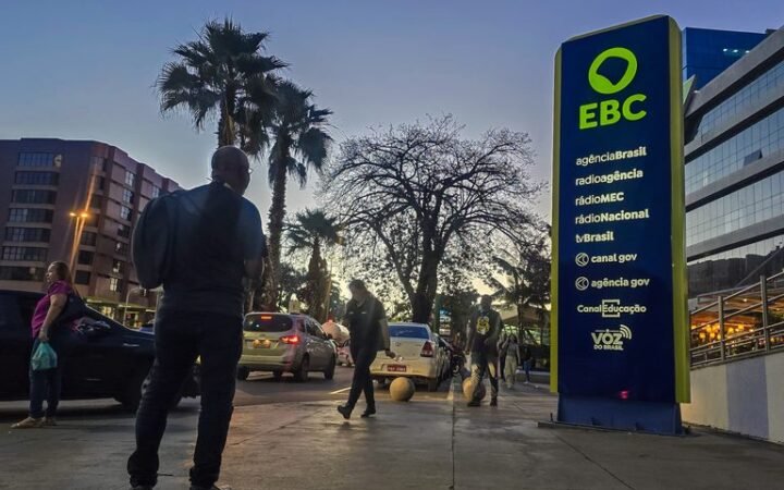 Pessoas caminham diante de prédio e placa institucional da EBC, em imagem de divulgação.