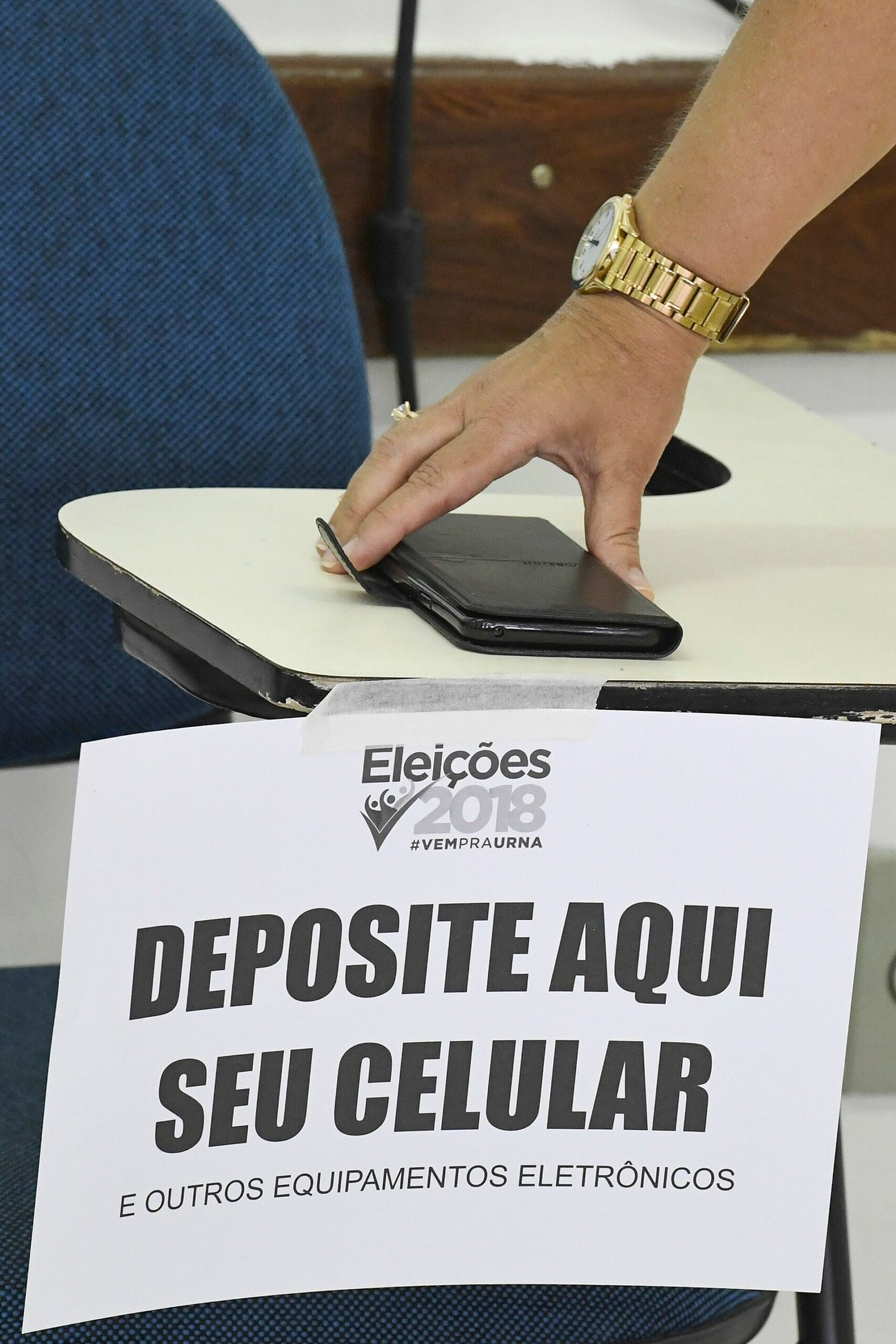 Pessoa deixa celular em caixa identificada para guardar aparelhos fora da cabine, nas eleições de 2018.