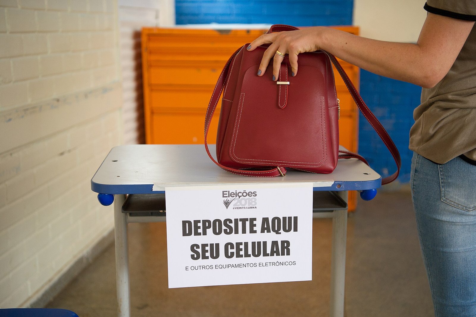 Eleitora ao lado de mesa com aviso para guardar celulares em seção eleitoral de 2018.