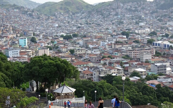 Vista de casas do Complexo do Alemão a partir da Igreja da Penha, com escadaria e visitantes em primeiro plano.
