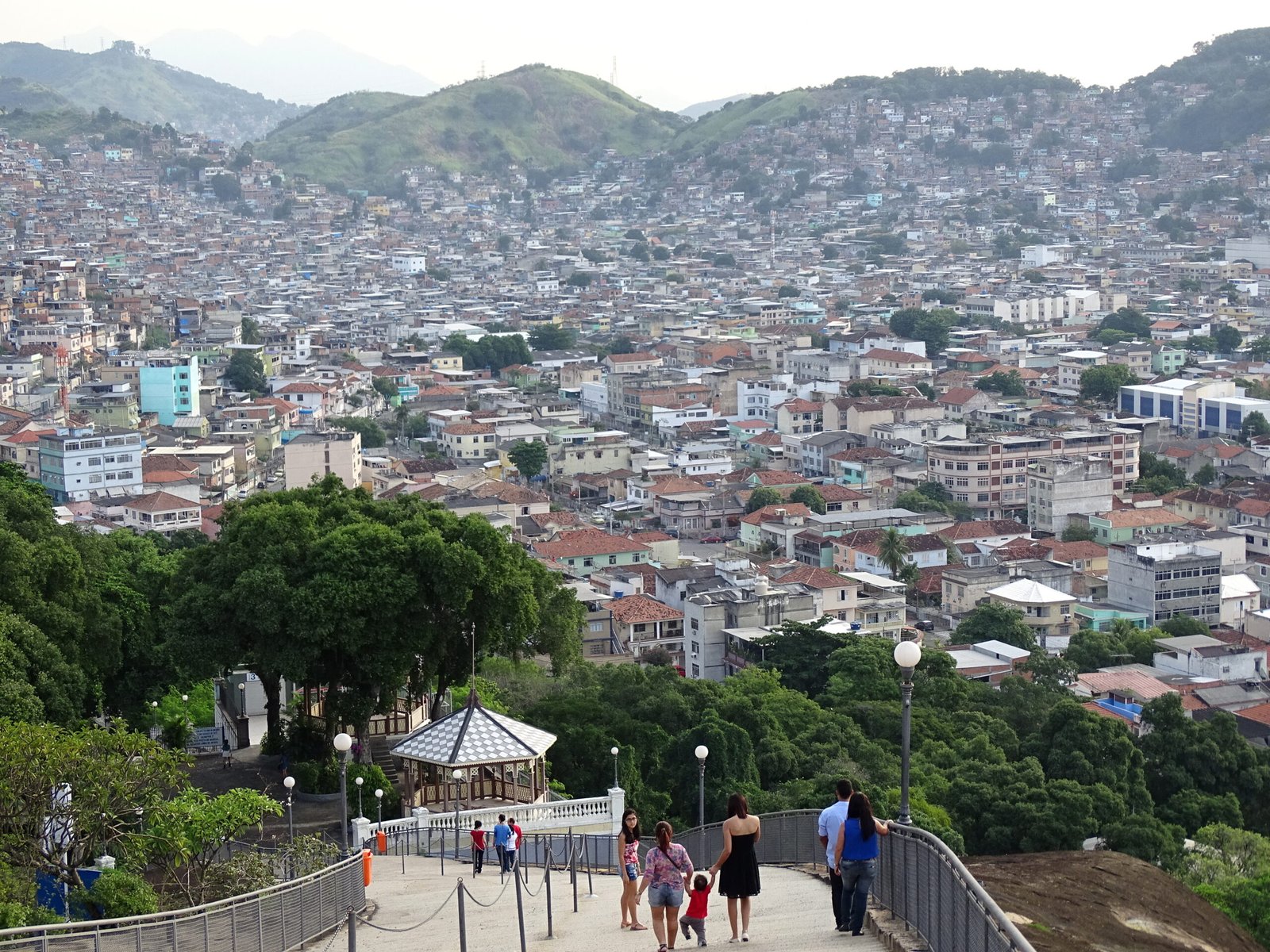 Vista de casas do Complexo do Alemão a partir da Igreja da Penha, com escadaria e visitantes em primeiro plano.