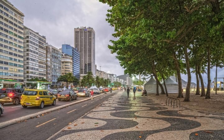Calçadão de Copacabana, árvores e avenida junto à orla, no Rio de Janeiro.