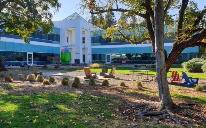Área externa colorida do Googleplex, em Mountain View, fotografada em 17 de novembro de 2019. Prédio com vidraças, árvores e cadeiras; imagem de arquivo de Misaochan2.