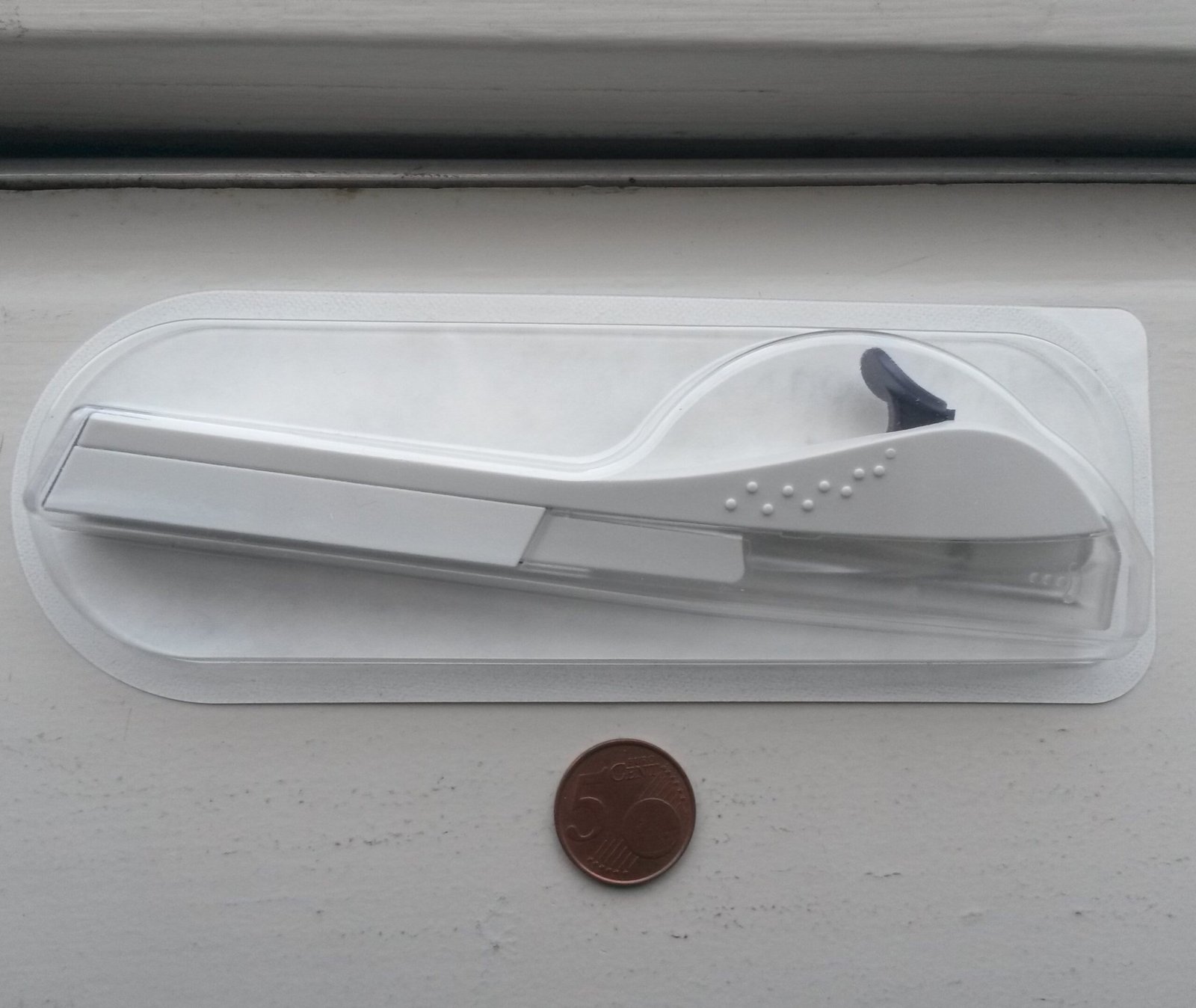 Aplicador de implante contraceptivo em embalagem transparente, com uma moeda para indicar a escala.