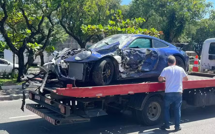 Carro esportivo azul com a dianteira danificada sobre um guincho.