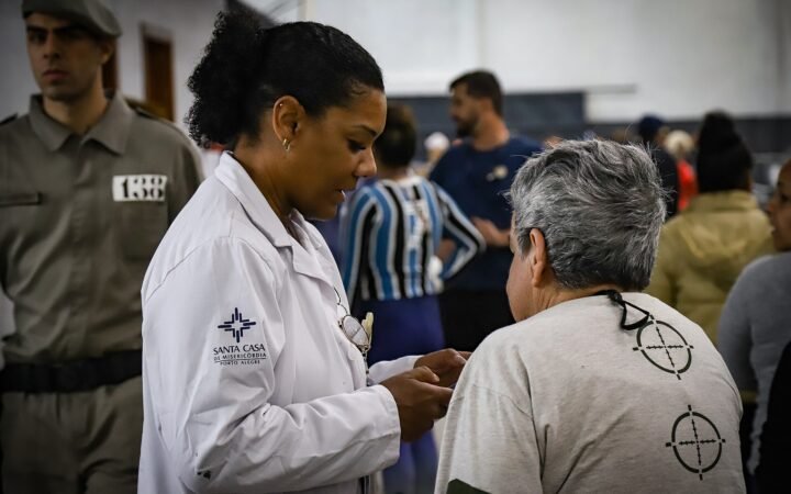 Profissional de saúde atende uma mulher em abrigo de Porto Alegre