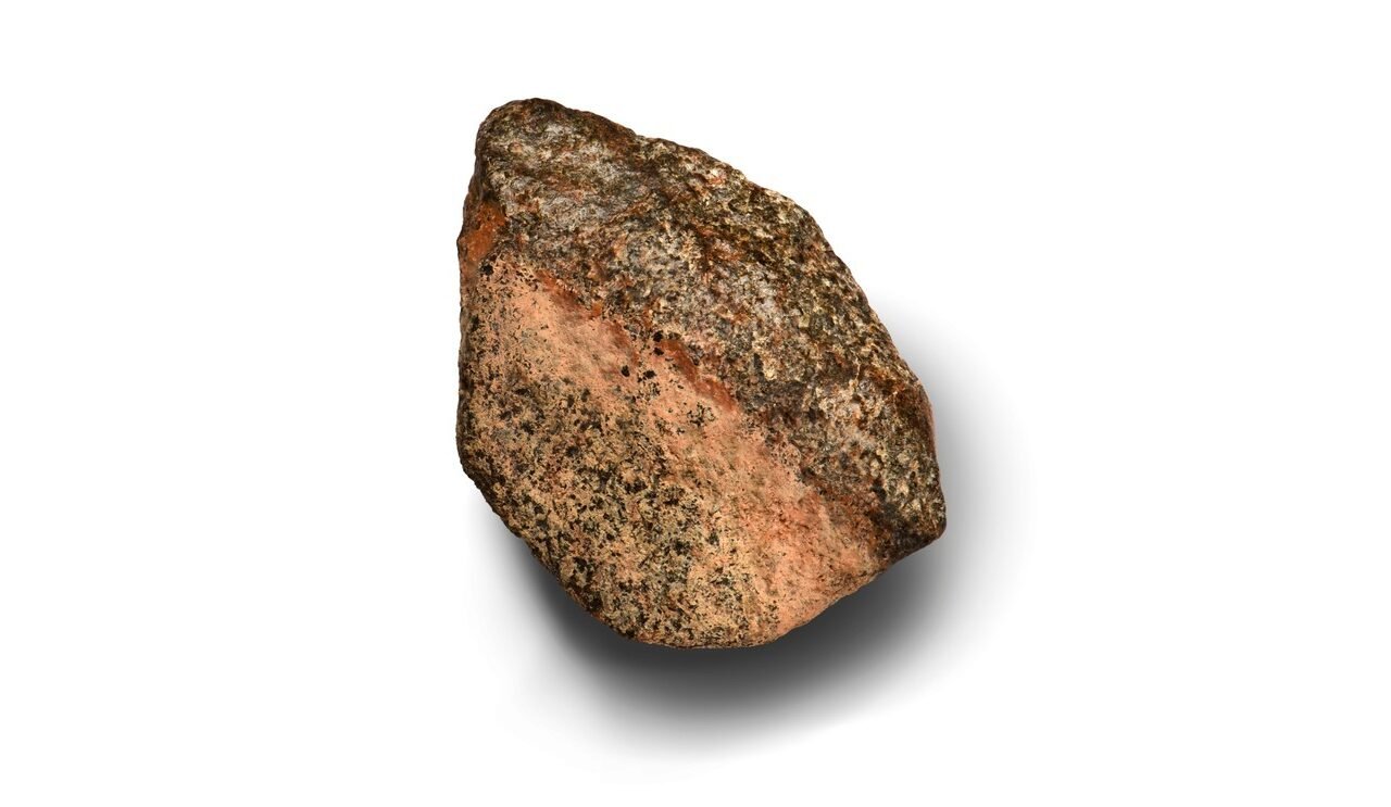 Meteorito Teghaza 001, com superfície rosada e minerais escuros, sobre fundo branco, em foto de divulgação do estudo de 29 de outubro de 2026.