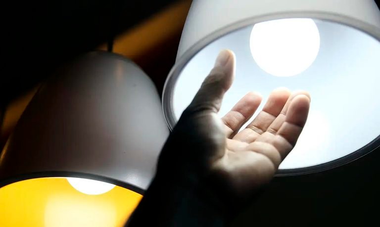 Mão próxima de lâmpada acesa, em fotografia de arquivo usada para ilustrar o custo da energia elétrica.