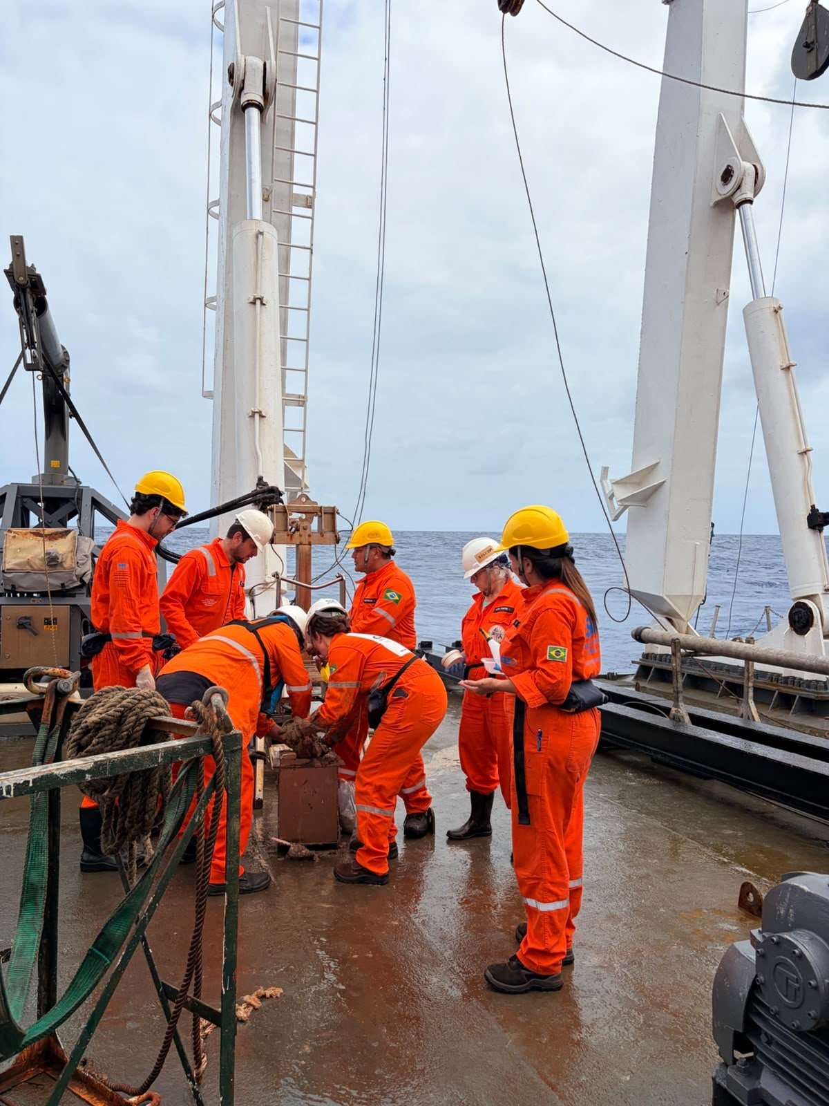 Pesquisadores de macacão laranja trabalham com equipamentos de amostragem a bordo do navio Vital de Oliveira.