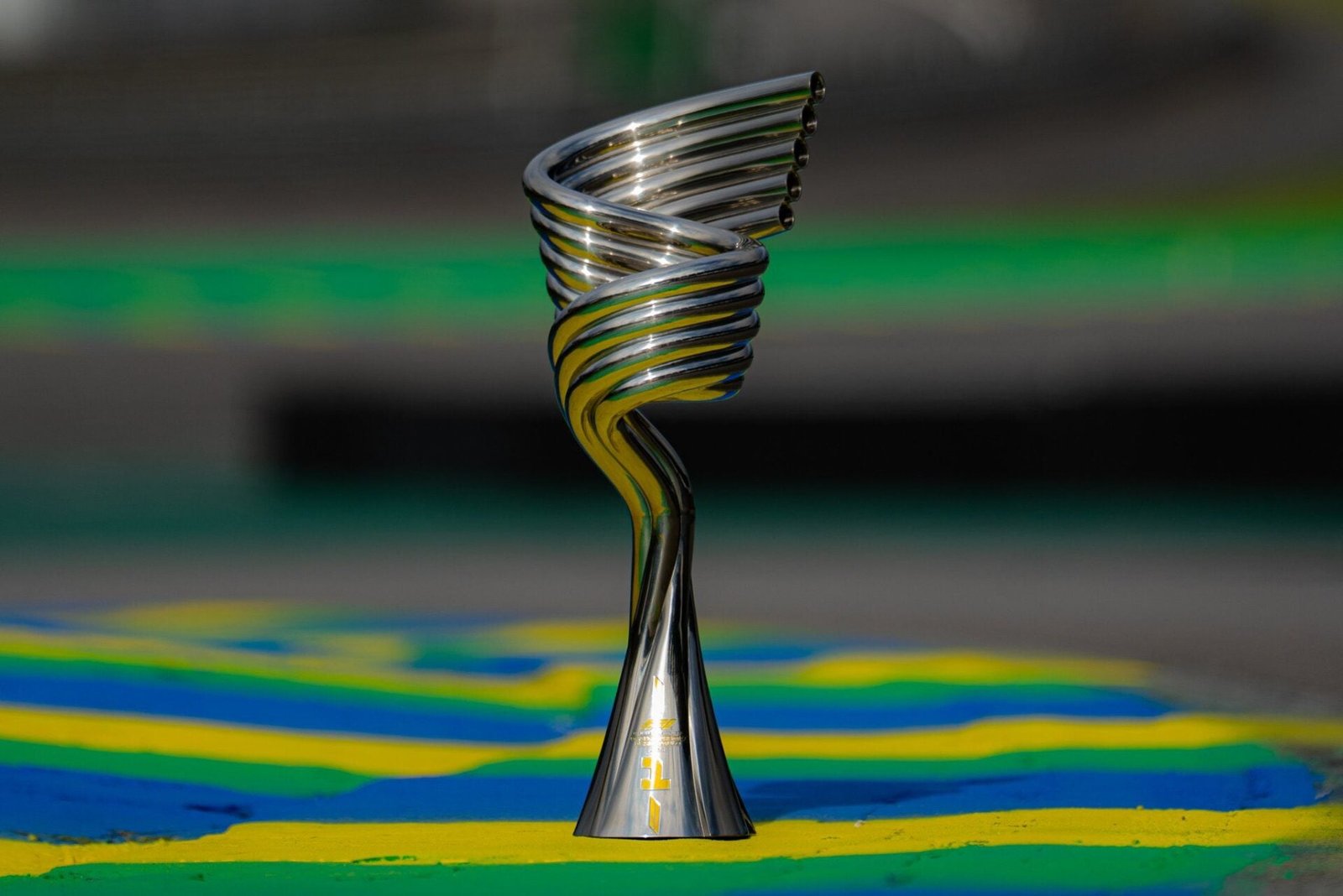 Troféu prateado do GP de São Paulo de 2026, com cinco tubos curvos, sobre uma zebra verde, amarela e azul de Interlagos